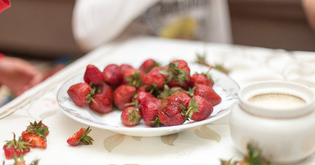 Sweet fresh strawberries on a plate on the table for, hands take and keep ripe red strawberries, a bunch of fresh strawberries in a ceramic bowl on a white table background