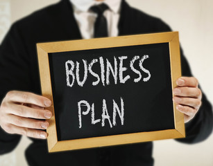 male businessman in a suit with tie holds in his hand a sign with the inscription BUSINESS PLAN