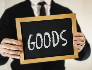 male businessman in a suit with tie holds in his hand a sign with the inscription GOODS