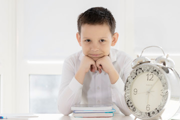 Back to school. Pupil drawing while sitting at the desk. Child in the class room. Alarm clock, pencils, books. Student boy from primary school. first day of fall.