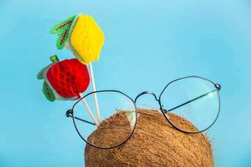 Whole brown coconut in shell in stylish glasses with topper decorated with fruits on a bright blue background