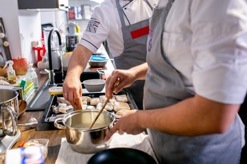 Cooks stir the ingredients in a saucepan and place the fish on a baking tray. Master class in the kitchen. The process of cooking. Step by step. Tutorial. Close-up