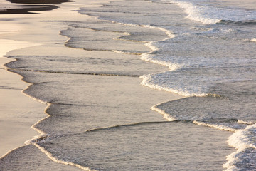 slow incoming Pacific waves at sunset with reflecting sunlight, Northland, New Zealand