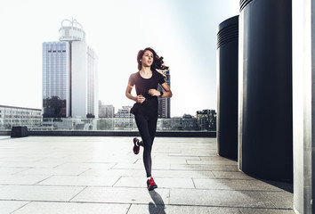 Young sporty woman running against urban background