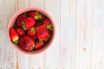 Red strawberry in a pink bowl on a light background.