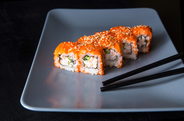 Sushi California Roll with crab meat, cucumber, masago, chopsticks on a gray plate, black background, side view