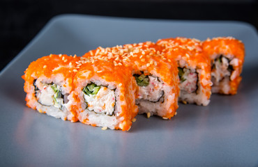 Sushi California Roll with crab meat, cucumber, masago on a gray plate, black background, close-up