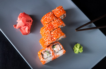 Sushi California Roll with crab meat, cucumber, masago, wasabi, chopsticks and ginger on a gray plate, black background, top view
