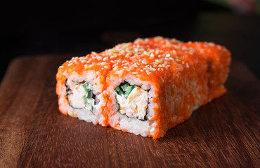 Sushi California Roll with crab meat, cucumber and masago on a wooden cutting board, black background, close-up