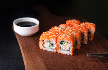 Sushi California Roll with crab meat, cucumber, masago and soy sauce on a wooden cutting board, black background, close-up