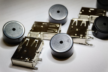 Close-up of scattered USB socket and buzzer electronics components on white background in partial focus and random pattern