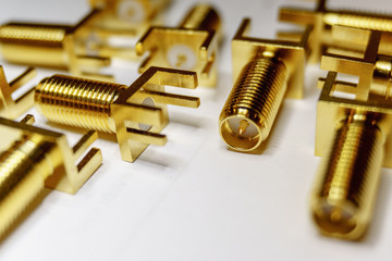 Close-up of scattered gold plated SMA male connectors electronics components in partial focus on white background in random pattern