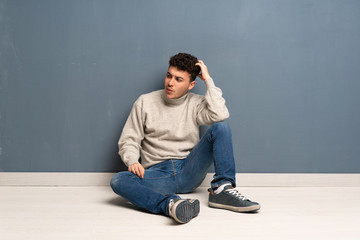 Young man sitting on the floor having doubts while scratching head