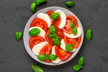 plate of italian caprese salad in a plate over dark concrete background. healthy food. top view