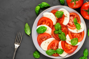 fresh italian caprese salad with sliced tomatoes, mozzarella cheese, basil, pepper and fork in a plate