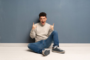 Young man sitting on the floor making rock gesture