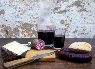Iberian pork sausages on an old wooden board with a wedge of sheep cheese, an antique knife and a bottle and a glass of red spanish wine
