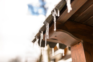 Hanging icicles from the roof of a wooden building on a winter frosty day, a lot of snow on the roof.