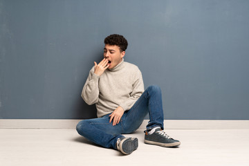 Young man sitting on the floor yawning and covering wide open mouth with hand
