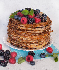 Pancakes on a platter with raspberries, blueberries and blackberries.  Lots of pancakes stacked. Thin pancakes with crispy crust. Carnival.