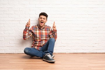 Young man sitting on the floor with fingers crossing