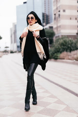 Beautiful and young girl in a coat and scarf and sunglasses walking around the city
