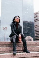 Trendy young woman in sunglasses sitting near stairs in the street