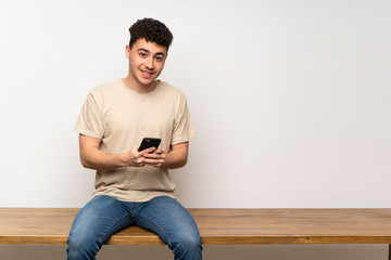 Young man sitting on table sending a message with the mobile