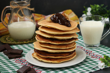 Pancakes with bananas on a plate against a dark background, behind is a jug and a glass of milk