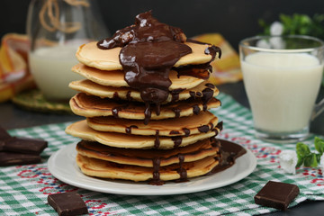 Pancakes with bananas on a plate against a dark background, behind is a jug and a glass of milk