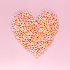 Top view of the multi-colored marshmallows which lies in the shape of a heart on a monochrome pink background copyspace, topview, mockup, flatlay