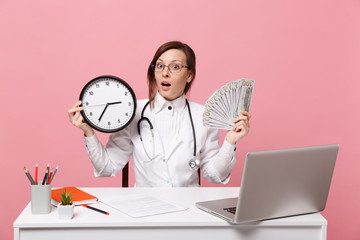 Female doctor sit at desk work on computer with medical document hold money in hospital isolated on...