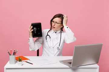 Female doctor sit at desk work on computer with medical document hold bank safe in hospital isolated on pastel pink background. Woman in medical gown glasses stethoscope. Healthcare medicine concept.
