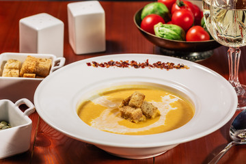 Spicy Pumpkin or lentil soup with cream an croutons in white plate on wooden background