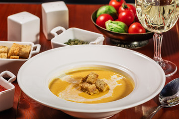 Spicy Pumpkin or lentil soup with cream an croutons in white plate on wooden background