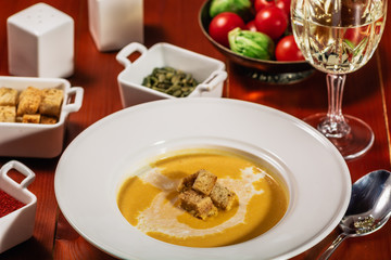 Spicy Pumpkin or lentil soup with cream an croutons in white plate on wooden background