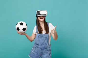 Smiling woman football fan in headset holding soccer ball, showing thumb up isolated on blue turquoise wall background. People emotions, sport family leisure lifestyle concept. Mock up copy space.