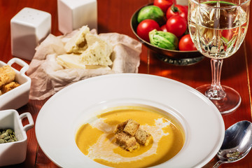 Roasted pumpkin and carrot soup with cream, pumpkin seeds. Served with croutons, cheese and white wine on wooden background. Copy space