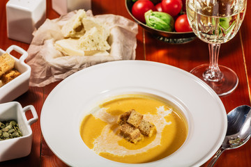 Roasted pumpkin and carrot soup with cream, pumpkin seeds. Served with croutons, cheese and white wine on wooden background. Copy space