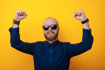 Bearded man wearing glasses  acts like he won something. Lucky young man isolated over yellow background
