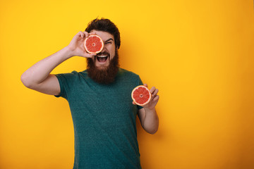 Bearded holding two halfs of grapefruit citrus fruit in hands, covering her eye with one