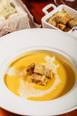 Dietary vegetarian pumpkin cream soup puree, served with white wine, pumpkin seeds, cheese and croutons, on brown wooden table, close up.