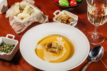 Pumpkin cream soup with croutons, baked chickpeas, sesame, parsley on a brown wooden background. Baked chickpeas with spices. Useful dietary snacks. Served with white wine and cheese