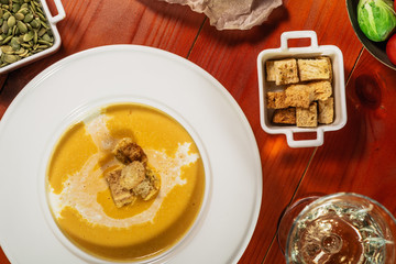 Traditional fall and winter dishes, hot and spicy pumpkin soup with pumpkin seeds, cream and croutons, on brown wooden table, served with white wine, copy space top view