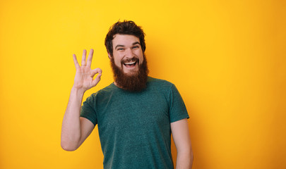 A handsome bearded man in tshirt isolated on yellow background showing ok sign, smiling broadly