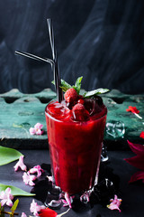 Cool fresh wild berries juice in glass with fruits, mint and straw on dark table background