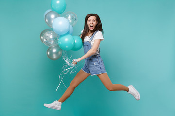 Excited young woman in denim clothes keeping mouth open, jumping high, celebrating holding colorful...