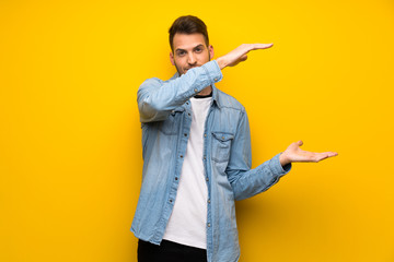 Handsome man over yellow wall holding copyspace to insert an ad