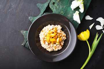 Top view of morning porridge with milk and delicious melon iin dark plate surrounded by tulips