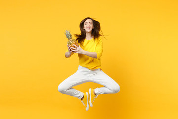 Fototapeta na wymiar Cute young woman in casual clothes keeping eyes clothes jumping hold fresh ripe pineapple fruit isolated on yellow orange background. People vivid lifestyle relax vacation concept. Mock up copy space.
